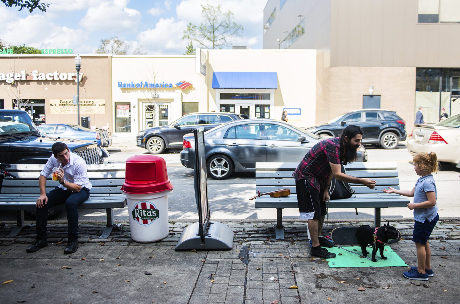 Street busker William Gomez hands a dog treat to a young passerby for his dog, Monica, a French bulldog, while playing his ukelele on Oct. 3, 2019, along Forbes Avenue in Squirrel Hill.
