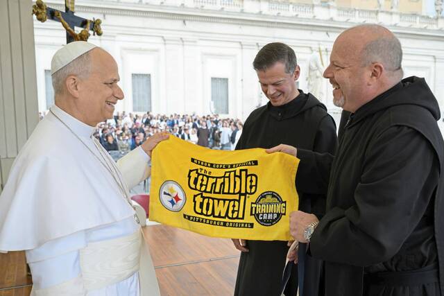 Pope Leo XIV smiles as he looks at the Saint Vincent College Training Camp edition of the Terrible Towel, presented during a May 13 visit to the Vatican by seminary rector the Very Rev. Edward Mazich and college president the Rev. Paul Taylor. (Courtesy Vatican Media)