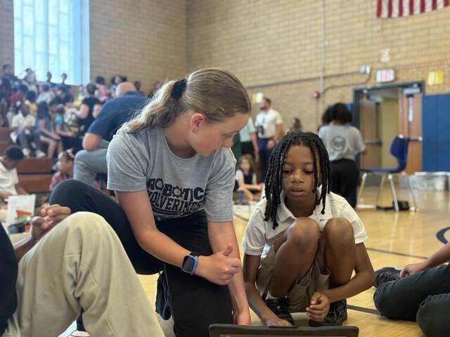 Piper Yoder, a sixth-grade student at Dickson Middle School in the Woodland Hills School District, works with Marqui Ellis, a third-grade student at Turtle Creek Elementary, during a robotics competition Thursday at Turtle Creek. (Kellen Stepler | TribLive)